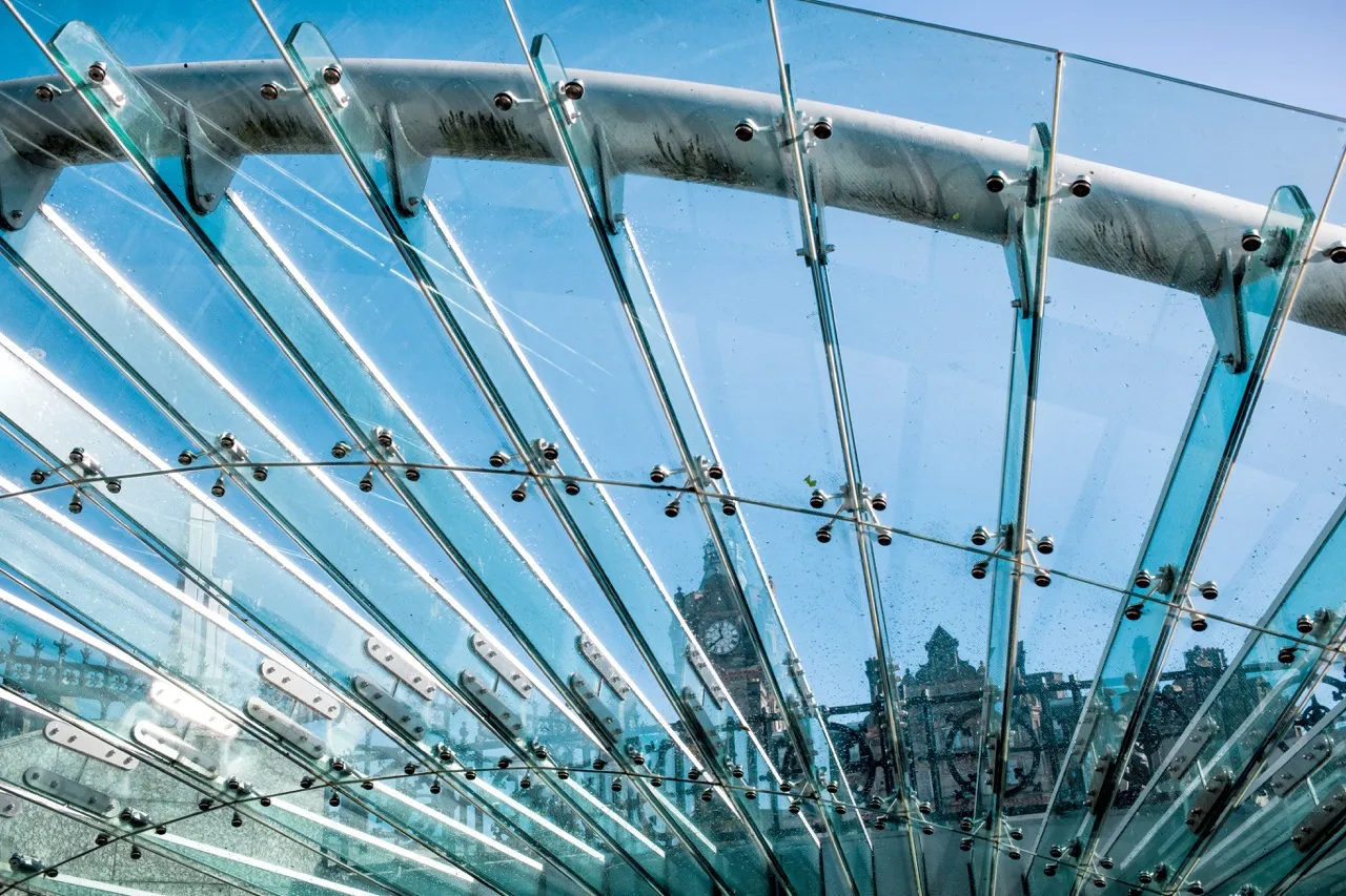 Exterior curved glass structure with metal fasteners under a clear blue sky.