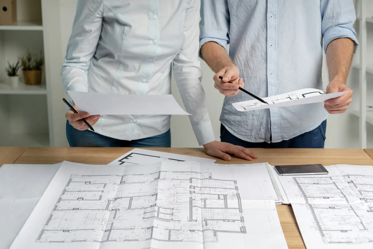Two people standing at a table reviewing commercial window blueprints.