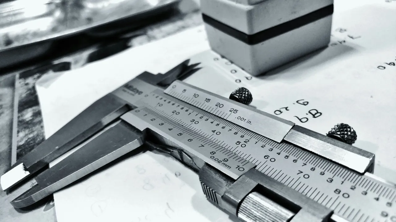 Close-up of a metal vernier caliper resting on papers with handwritten notes.