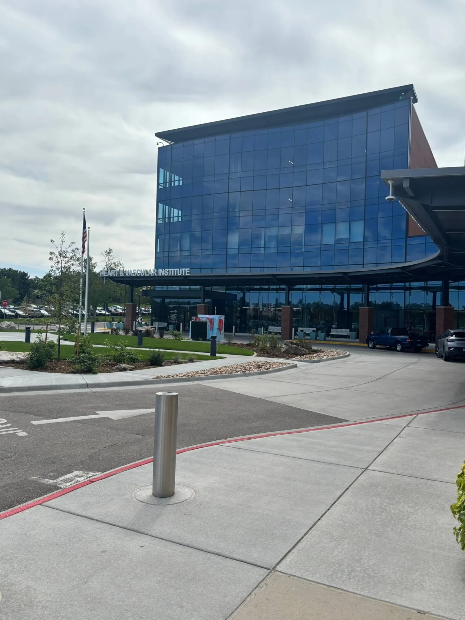 Modern glass building labeled Heart & Vascular Institute with a curved driveway and flagpole with an American flag.