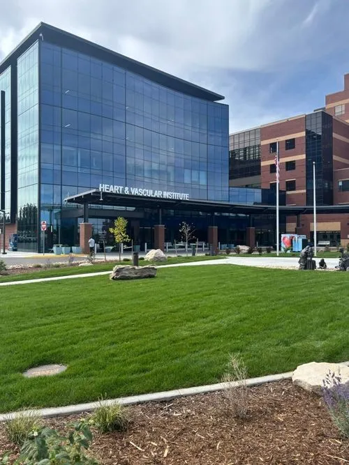 Modern Heart & Vascular Institute building with glass facade, green lawn, and sculptures in front.