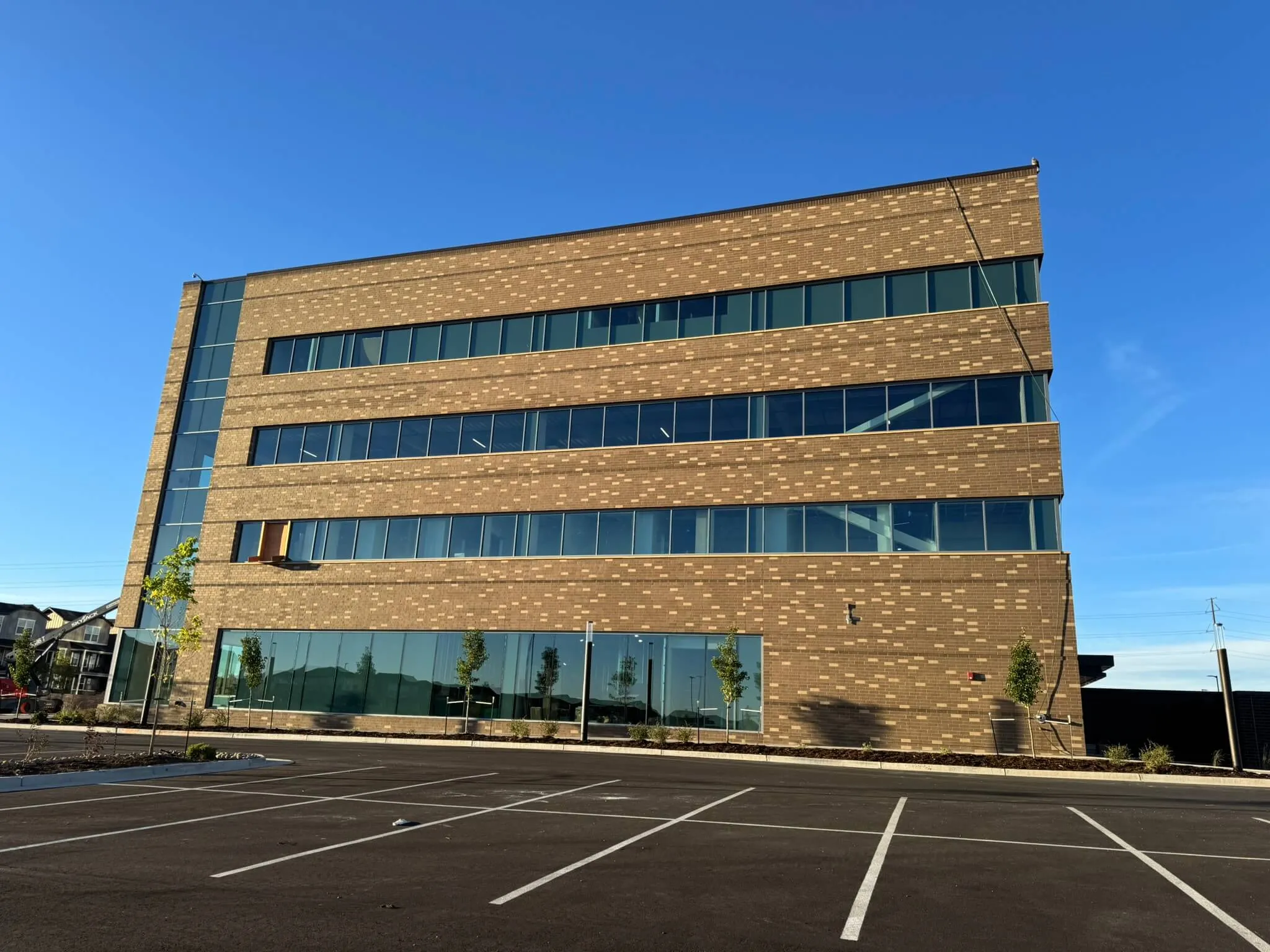 Modern four-story office building with large glass windows and a brick facade under a clear blue sky.