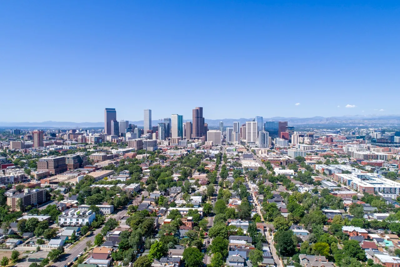 Aerial view of Denver city skyline with tall buildings and residential neighborhood under a clear blue sky.