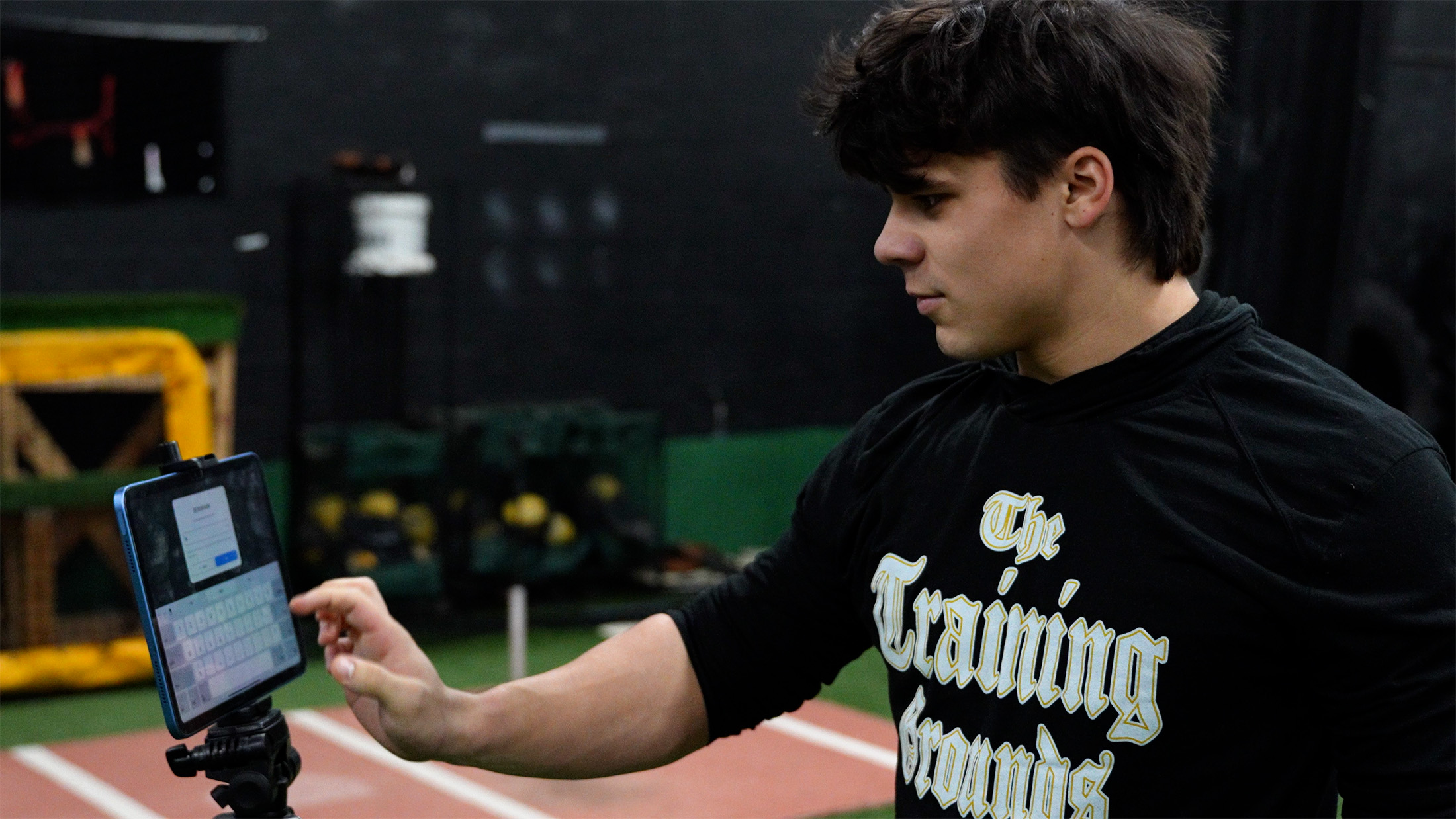People walking on a paved path on a sunny day near a baseball area, some carrying baseball bags and equipment.