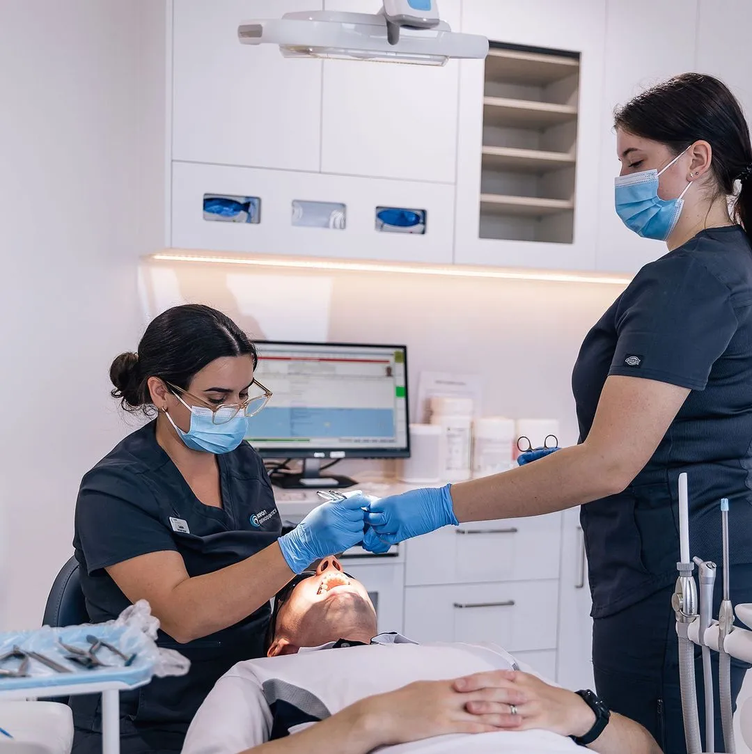 Dentist and dental assistant wearing masks and gloves treating a patient lying in the dental chair.
