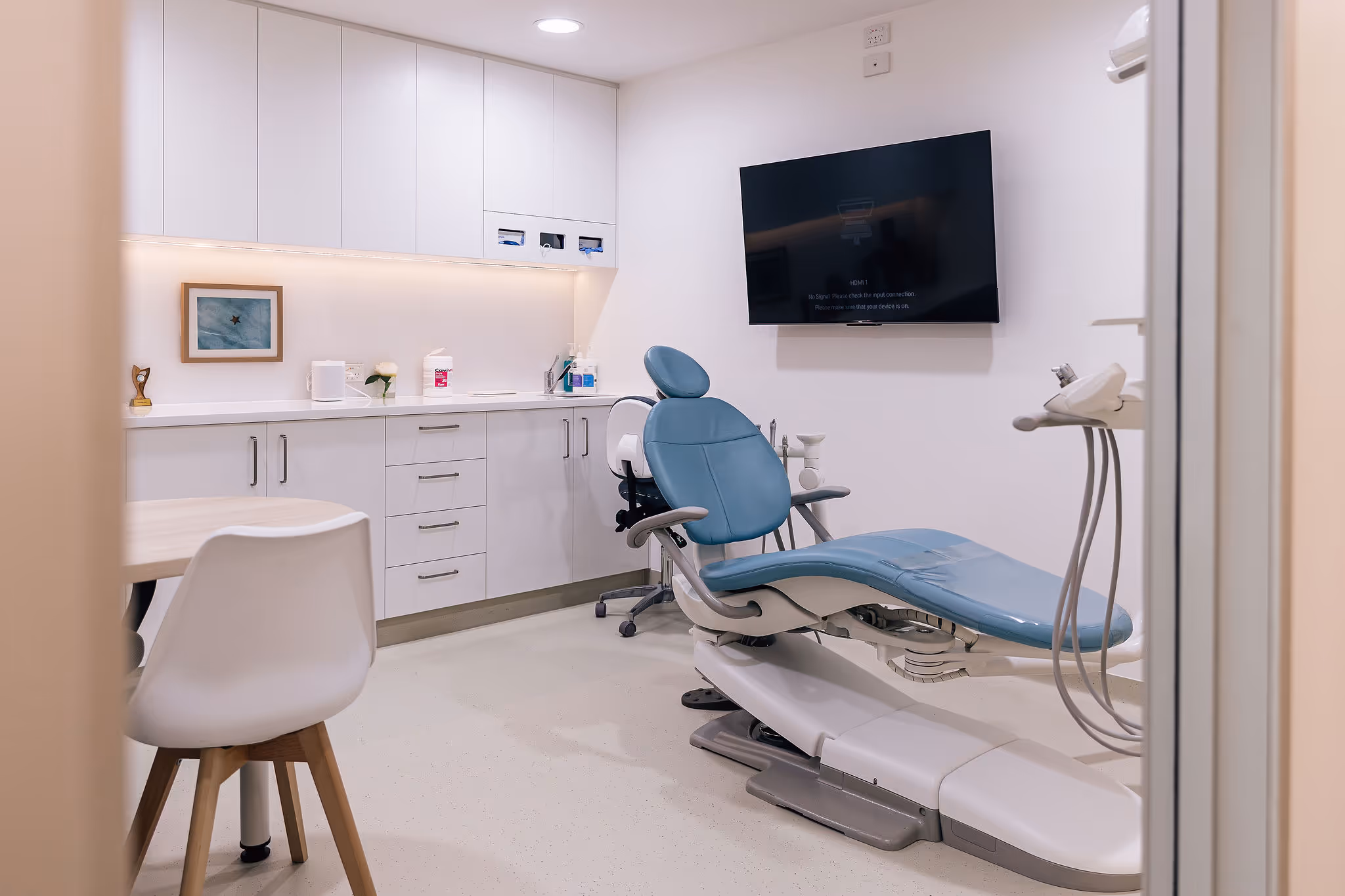 A dentist's surgery with a blue chair and a flat screen tv.