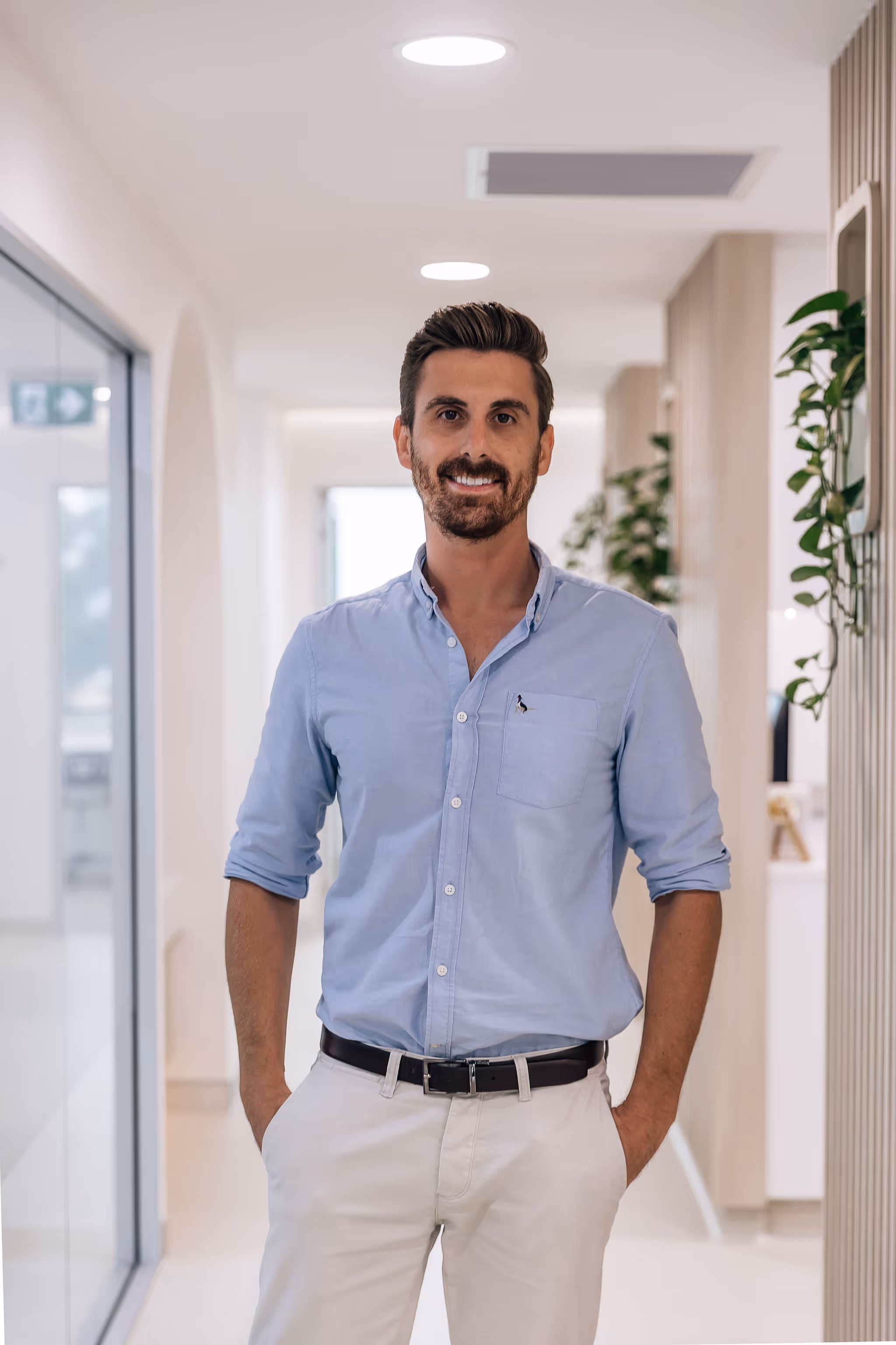 A man standing in the hallway of a dental practice with his hands in his pockets.