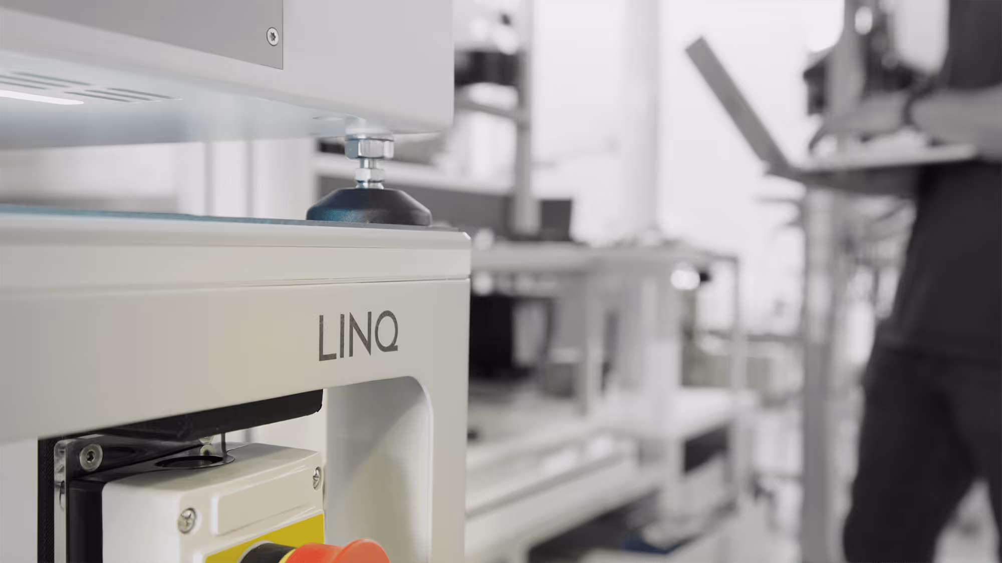 Close-up of industrial machinery labeled LINQ with blurred person using a laptop in the background.