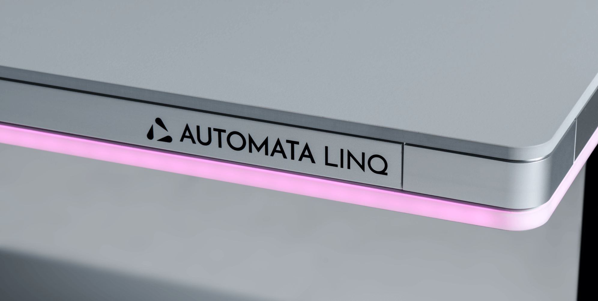 Close-up of a silver metal surface with a black Automata Linq logo and a glowing pink light strip beneath the edge.