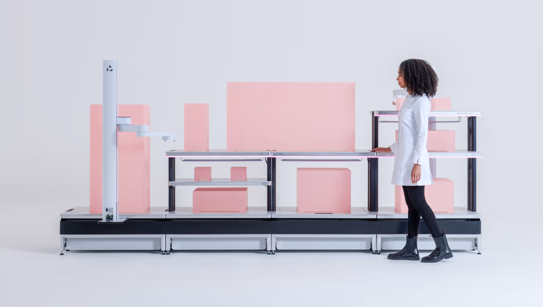 Woman in lab coat standing next to a modern automated workcell with pink blocks on the platform.