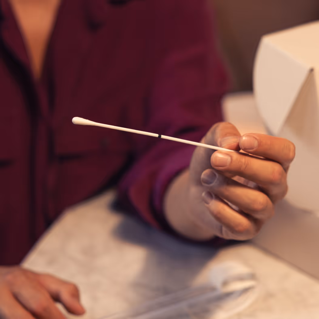 Close-up of a hand holding a cotton swab for at-home STI testing, with a test kit box in the background.