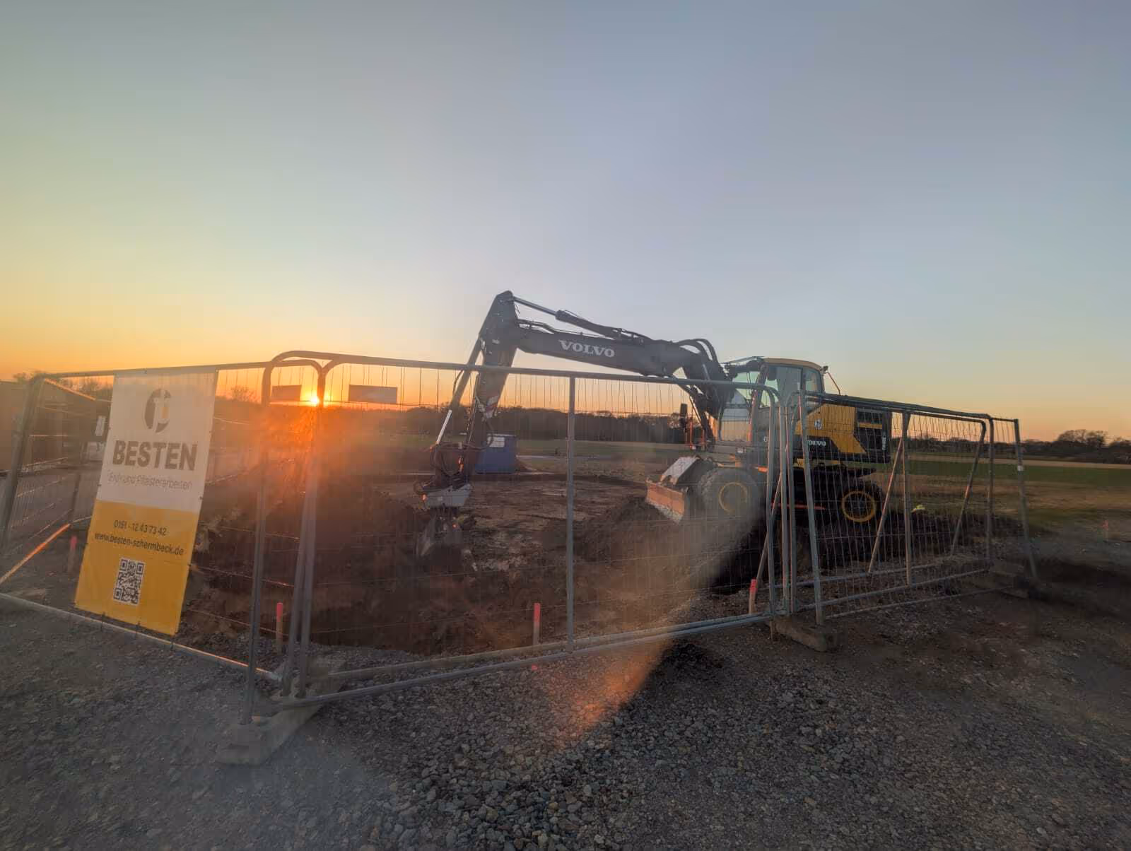 Baustelle von BESTEN bei Sonnenuntergang mit Volvo-Bagger hinter Bauzaun