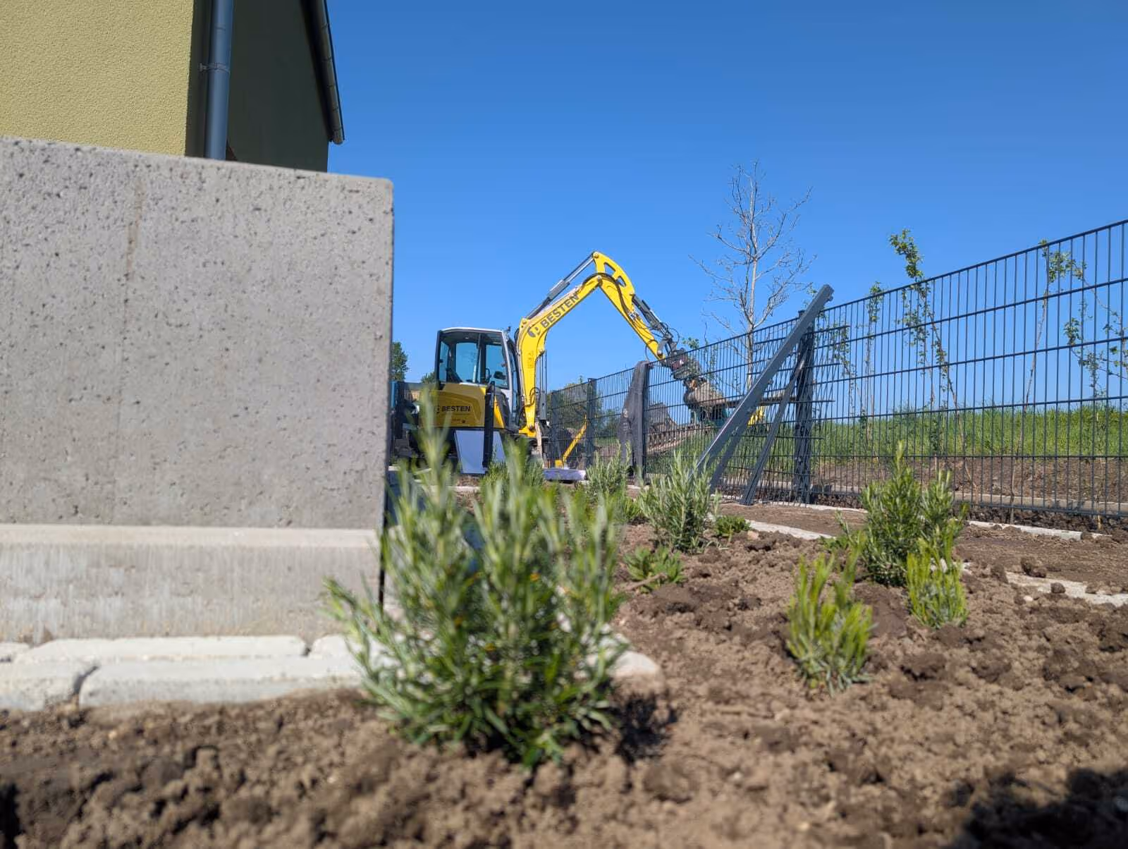 BESTEN-Bagger führt Garten- und Landschaftsbauarbeiten neben Haus mit Zaun durch
