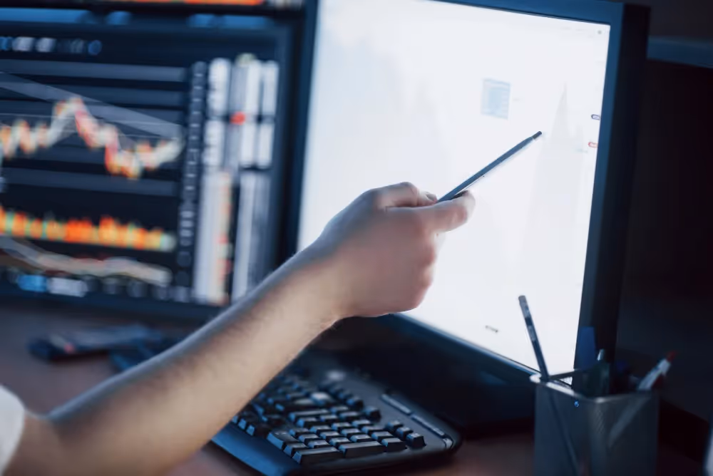 Bildschirm mit Aktien und jemand der mit einem Stift darauf zeigt