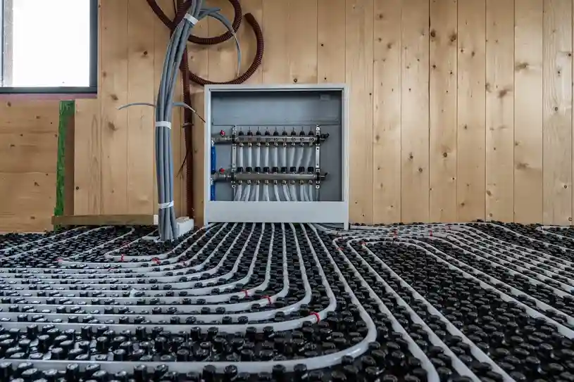 Underfloor radiant heating manifold mounted on a wooden wall with multiple connected PEX pipe loops.