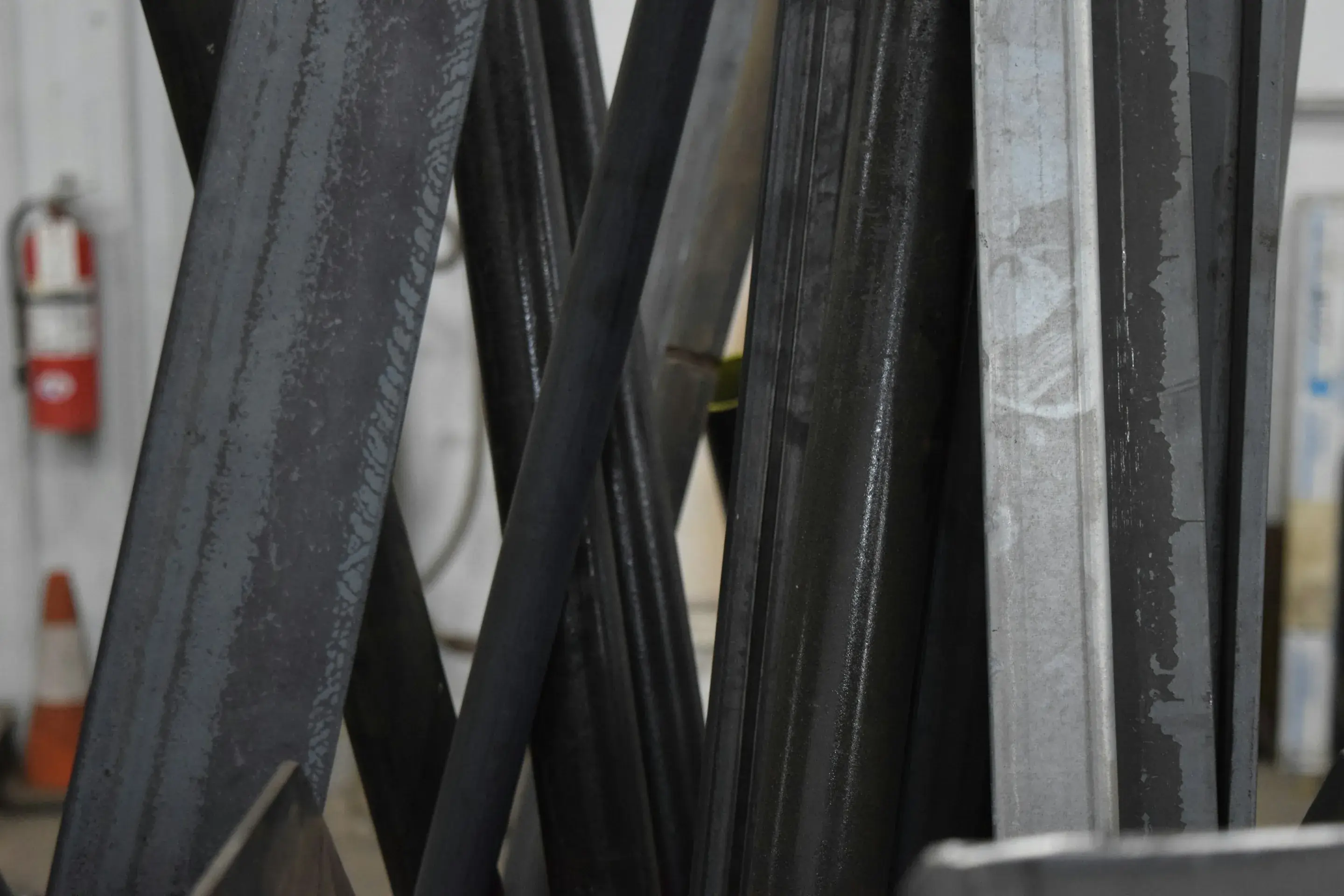 Stack of long, freshly cut dark metal bars and galvanized steel profiles leaning against each other in a workshop.