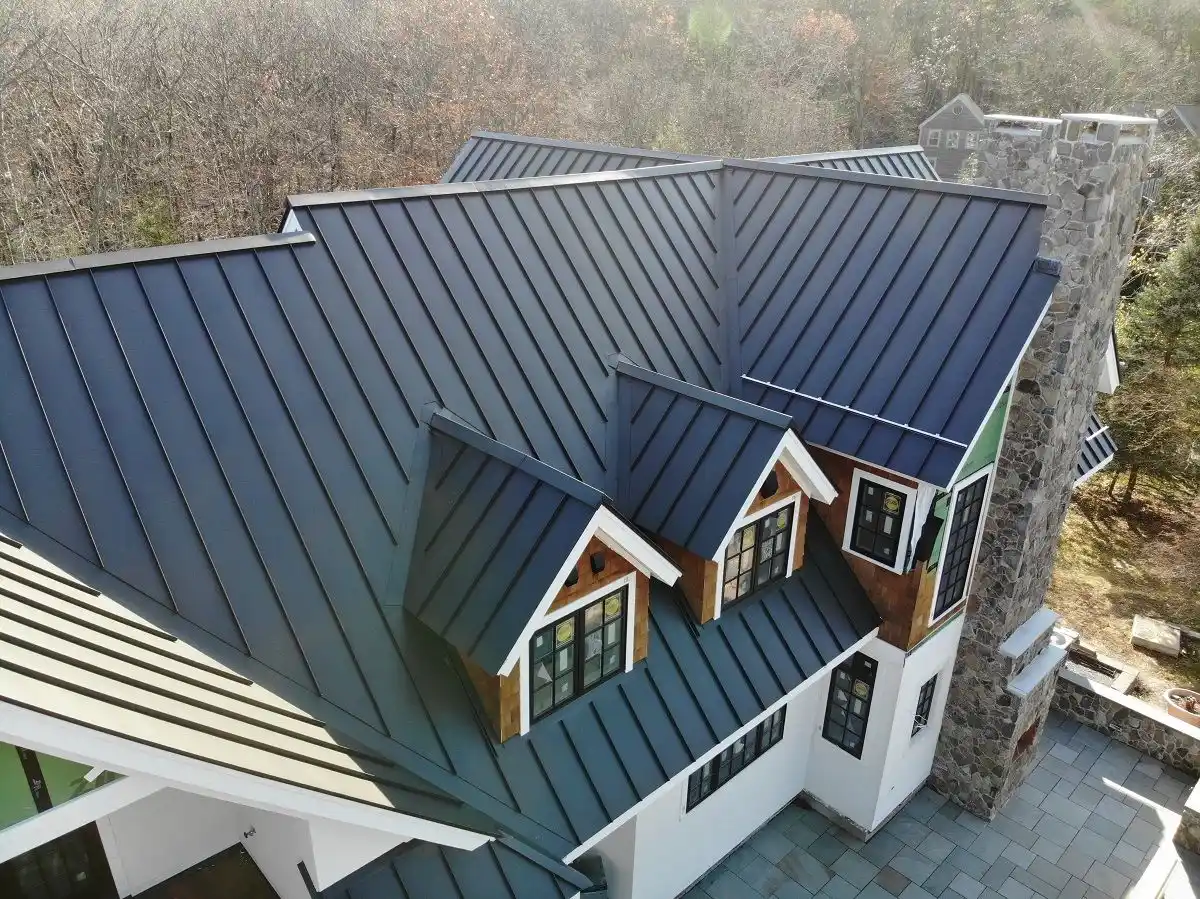 Steep dark charcoal metal roofing panels on a luxurious multi-gabled wooden mountain home with stone tower and forest surroundings.