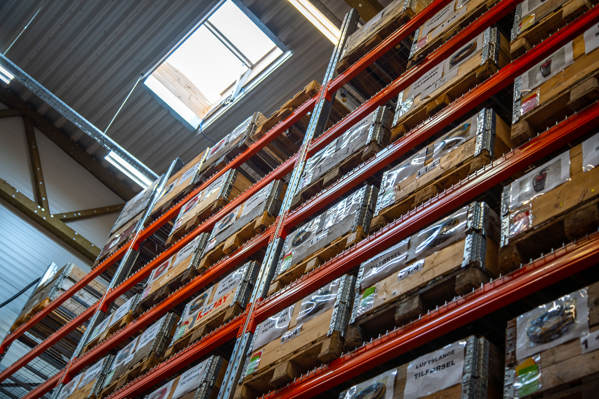Høyt lagerreol med stablede trepaller merket og organisert i et lyst lagerrom.