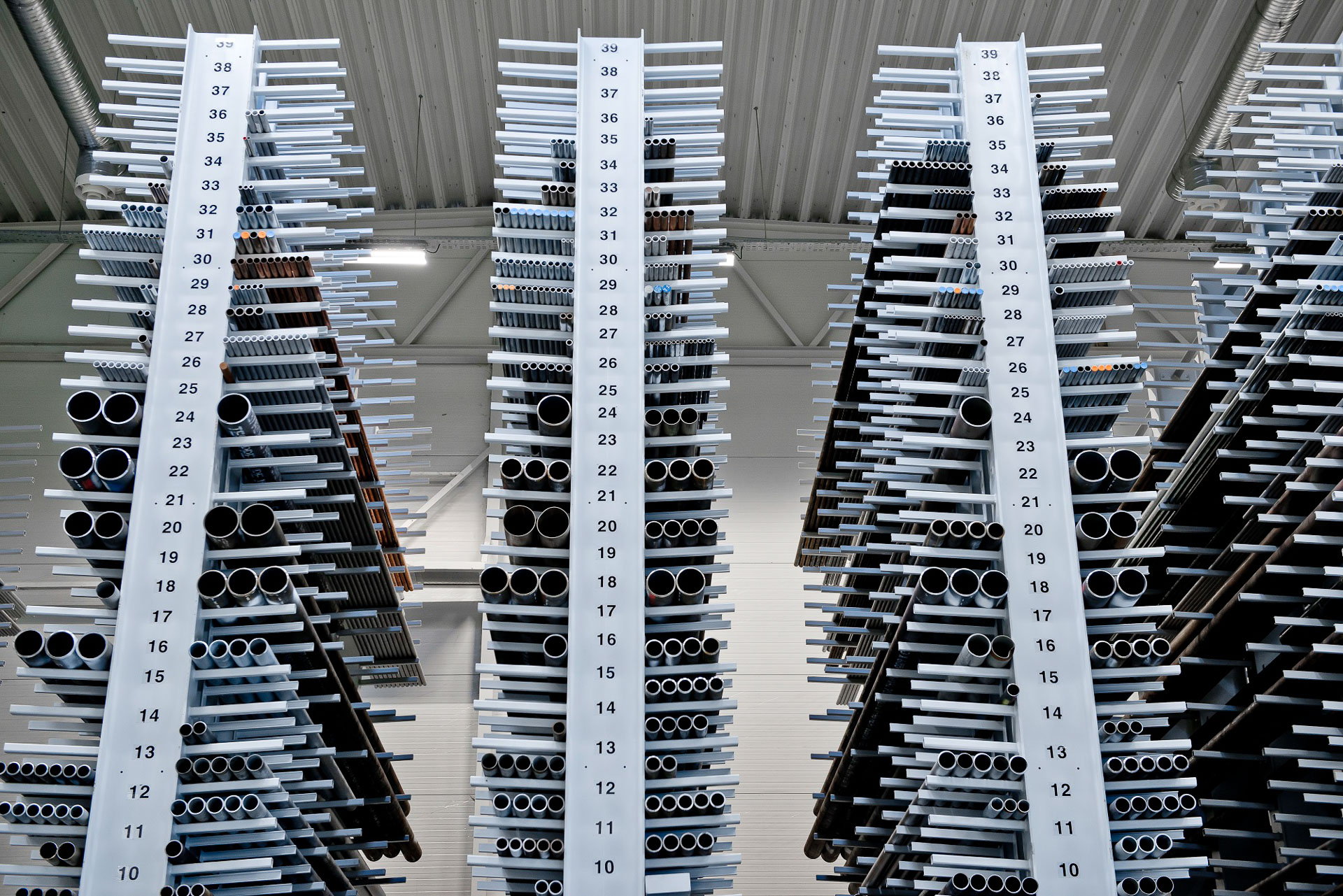 Metallrør i forskjellige størrelser organisert og lagret på høye stativer merket med nummer fra 10 til 39 i et lager.