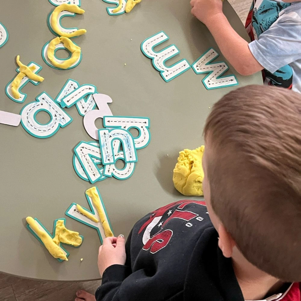 A young boy sitting at a table making letters.