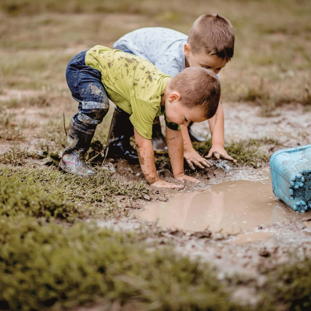 Two young boys playing in a muddy puddle.