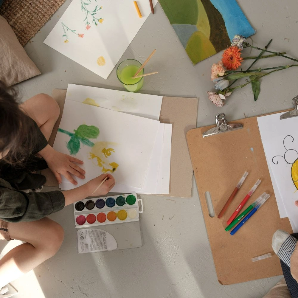 A little girl sitting at a table with some art supplies.