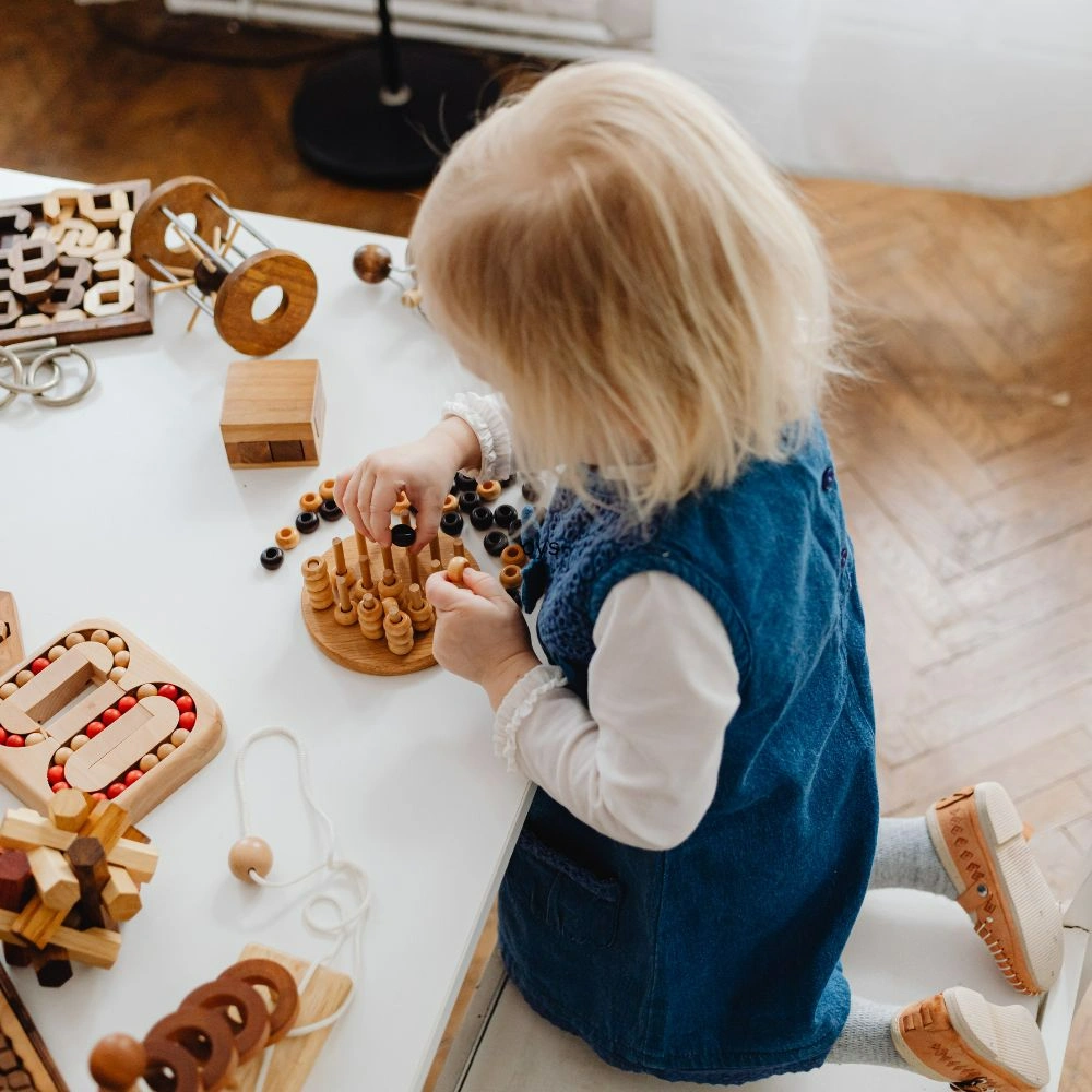 A little girl playing with wooden toys on a table.
