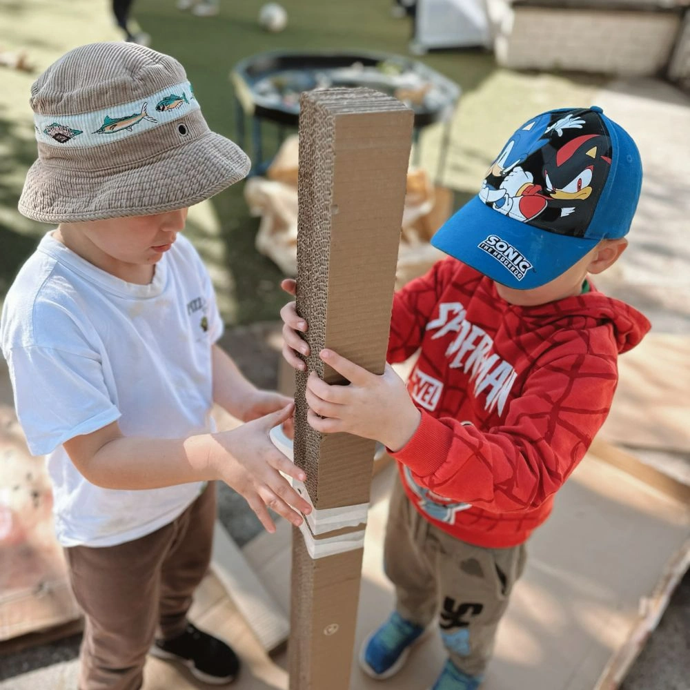 Two young boys standing next to each other near a cardboard box.