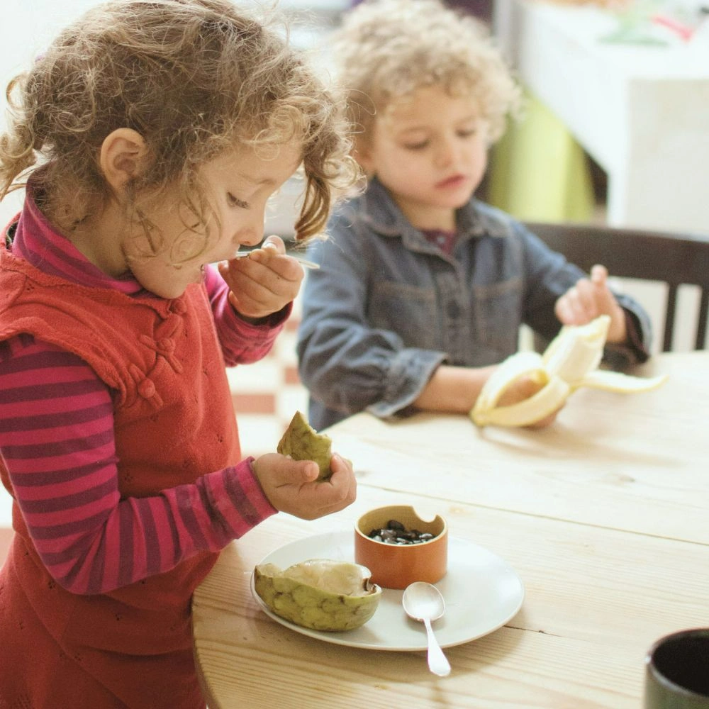Two children sitting at a table eating food.