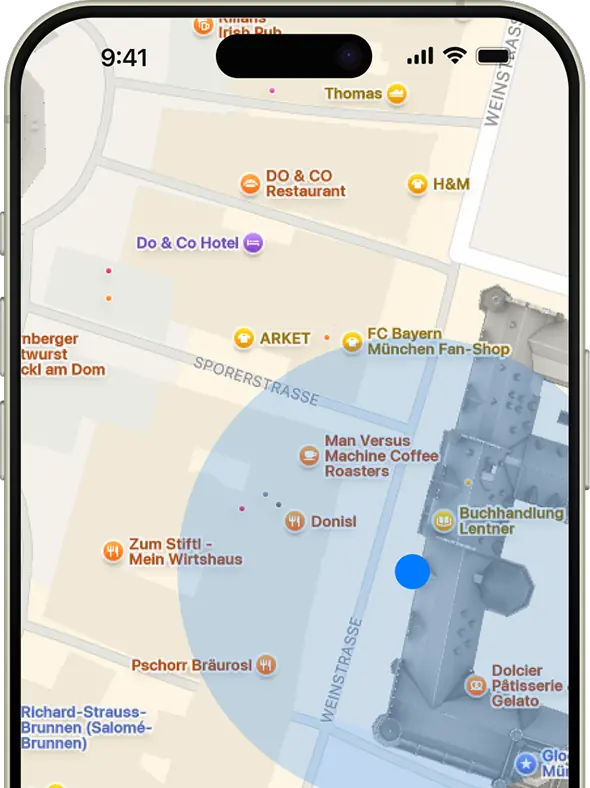 Map view on a smartphone screen showing businesses like DO & CO Restaurant, FC Bayern München Fan-Shop, Man Versus Machine Coffee Roasters, and Zum Stiftl - Mein Wirtshaus in a city area with a blue dot indicating current location.