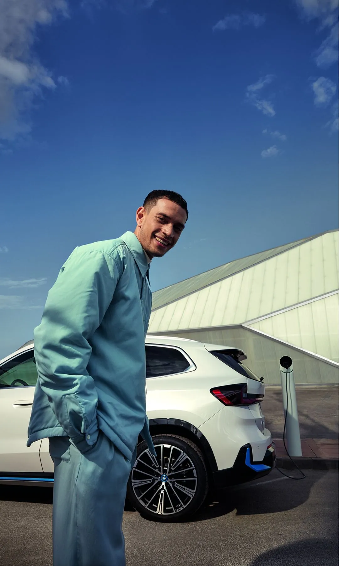 Person smiling in front of a white BMW car that's charging