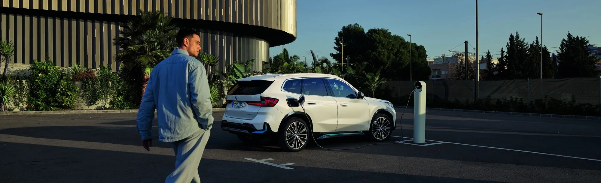 A person walking towards a white BMW SUV that's charging