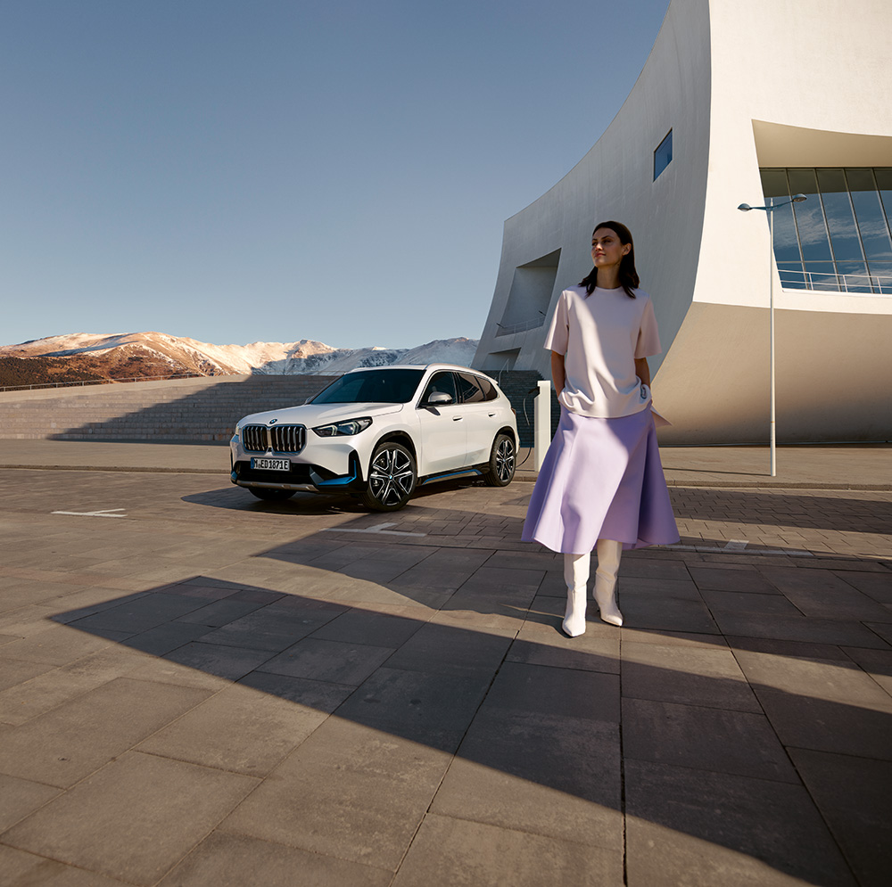 Person posing in front of a white BMW SUV