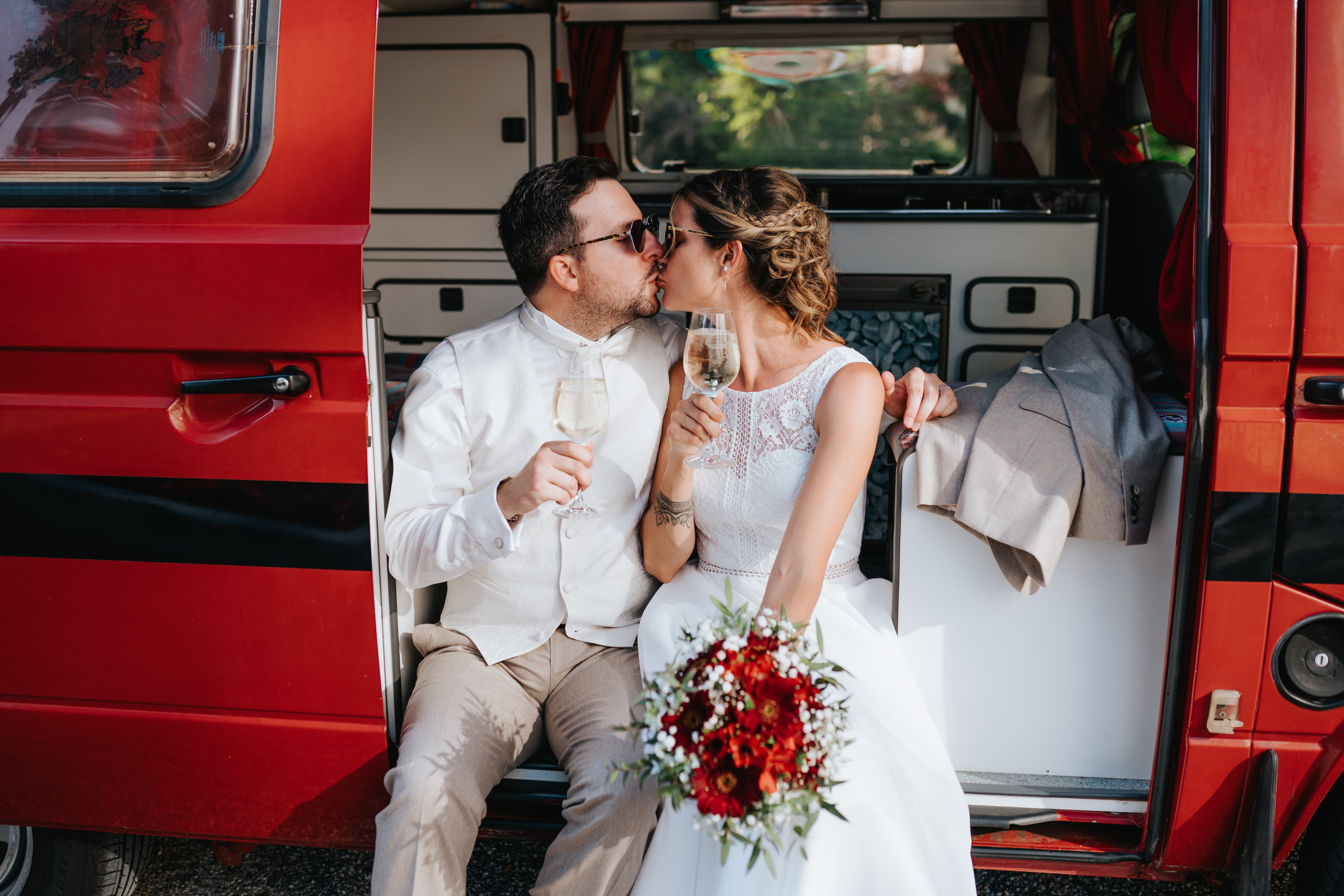 Glückliches Brautpaar küsst sich mit Weingläsern in der Hand