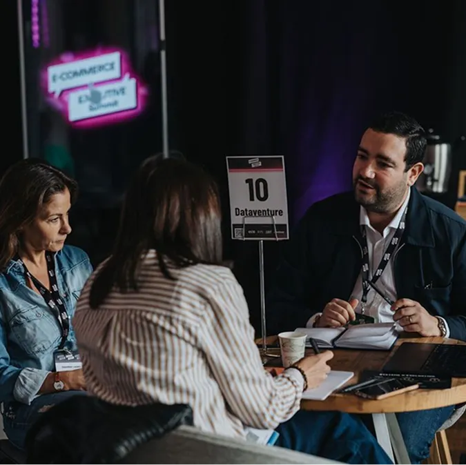 Three people seated around a table engaged in discussion at a Dataventure event, with a sign displaying '10 Dataventure'.