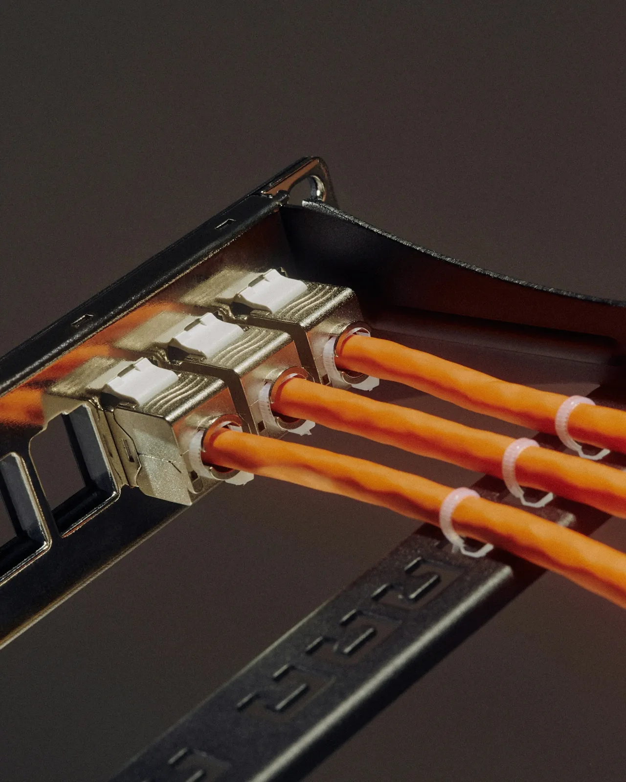 Three orange fiber optic cables connected to a metal network interface card.