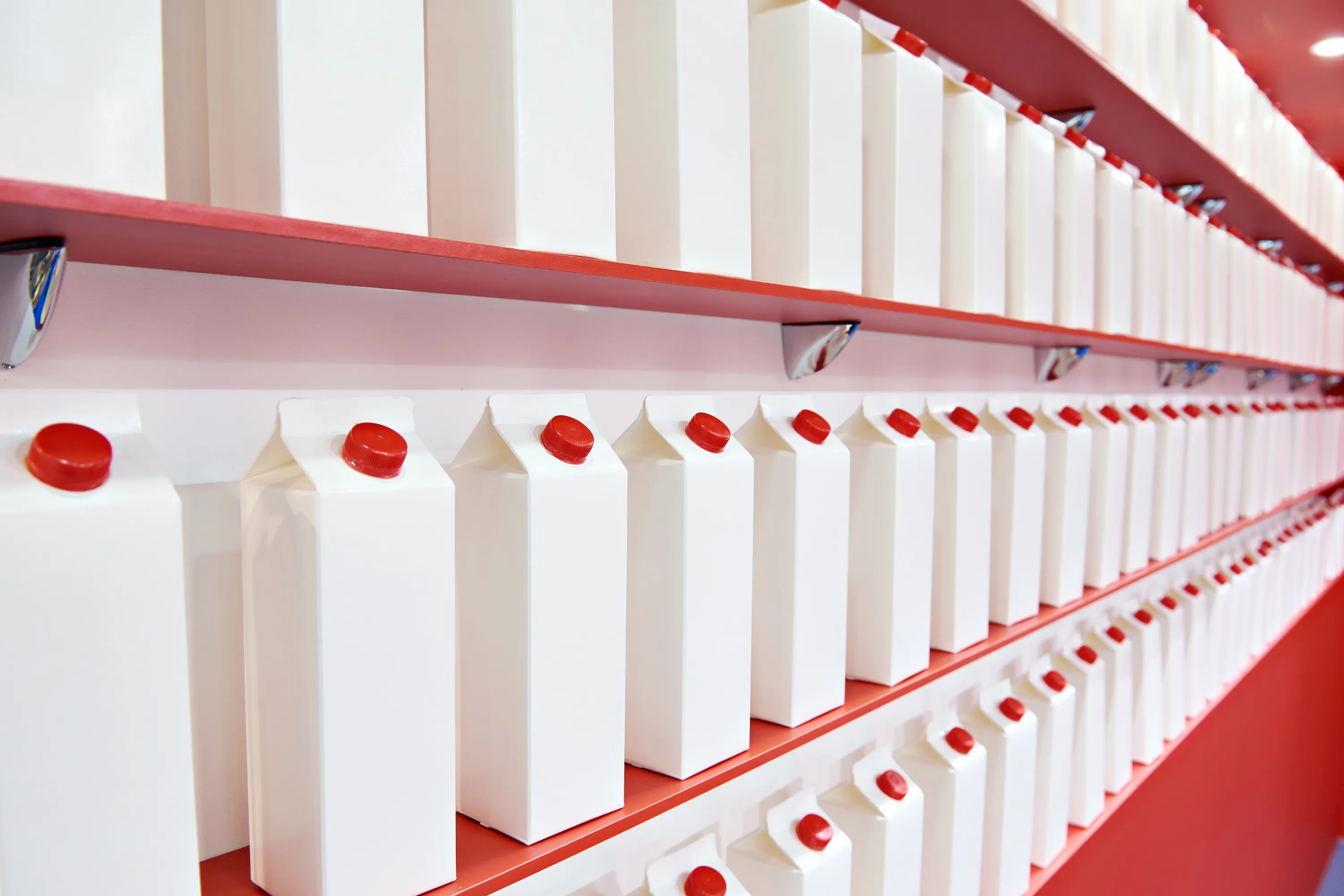 Rows of white cartons with red caps neatly arranged on red shelves.