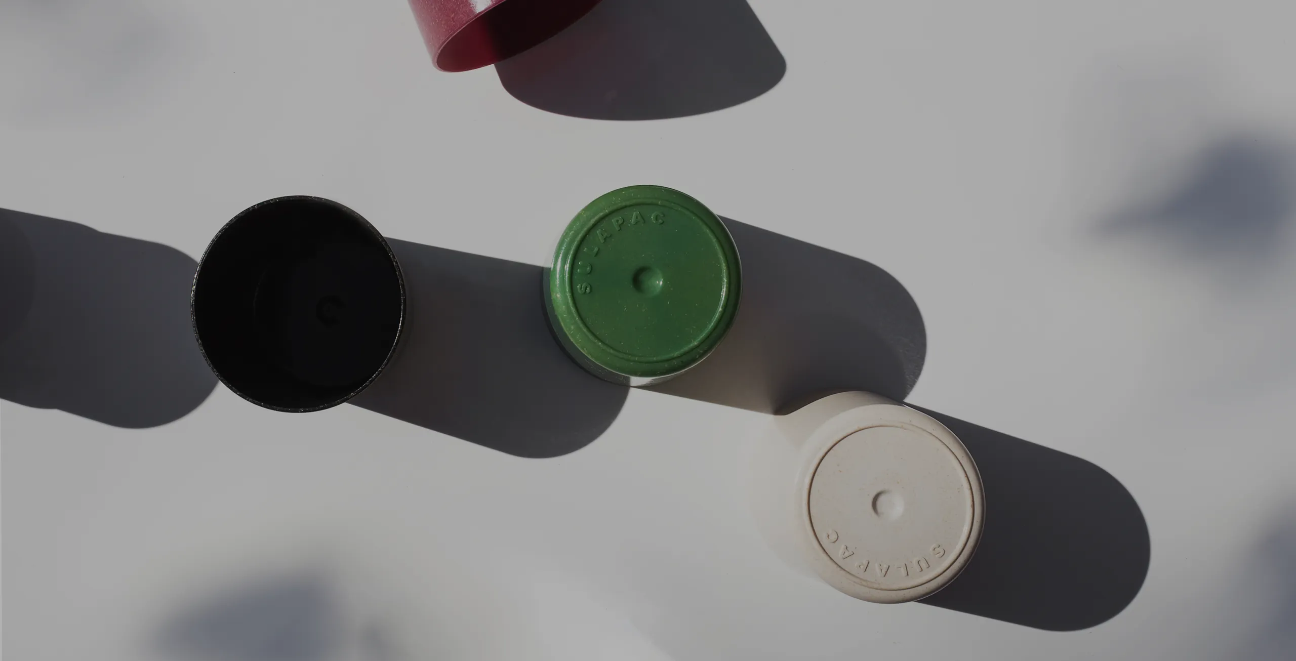 Eco-friendly cosmetic jar lids in black, green, and beige with shadows.

