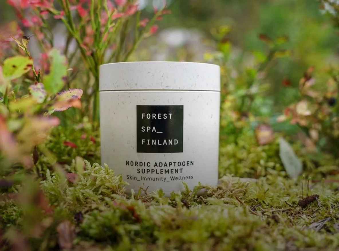 Eco-friendly supplement container labeled "Forest Spa Finland – Nordic Adaptogen Supplement" placed on moss in a natural setting.
