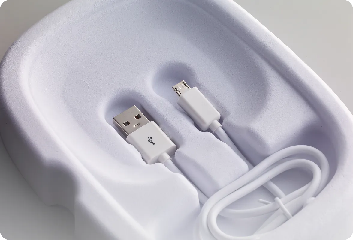 White PaperFoam packaging tray holding a USB charging cable, showcasing a sustainable and eco-friendly alternative to plastic packaging.