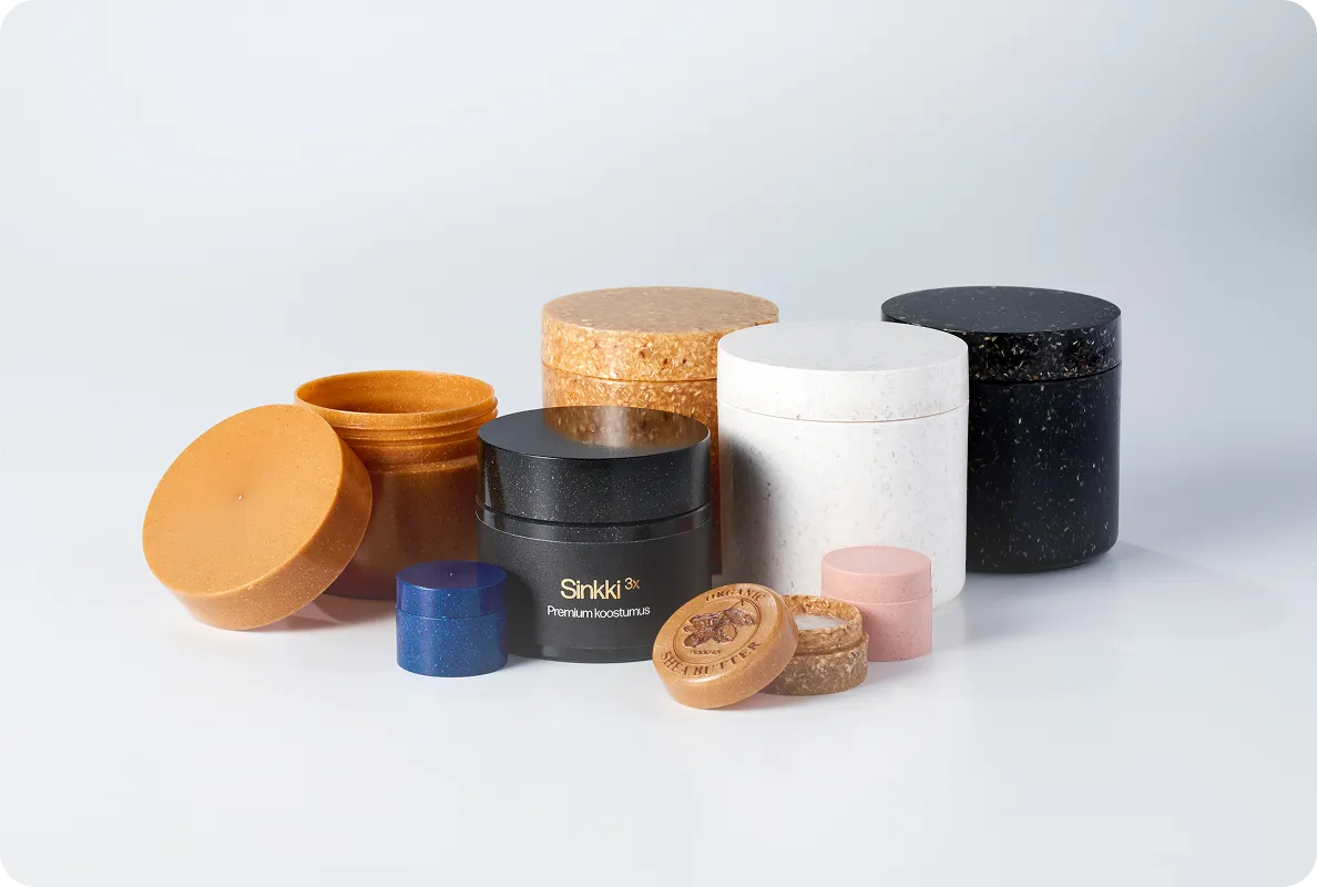 Collection of colorful eco-friendly cosmetic containers in various sizes and finishes, including black, white, brown, and natural textures.
