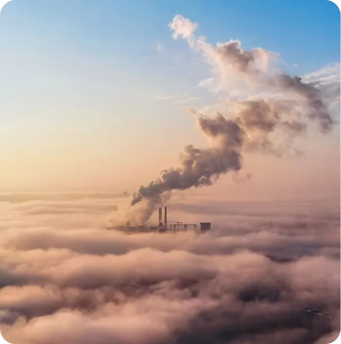 Industrial chimneys emitting smoke over a fog-covered landscape, symbolizing air pollution and the importance of sustainable, low-emission manufacturing solutions.