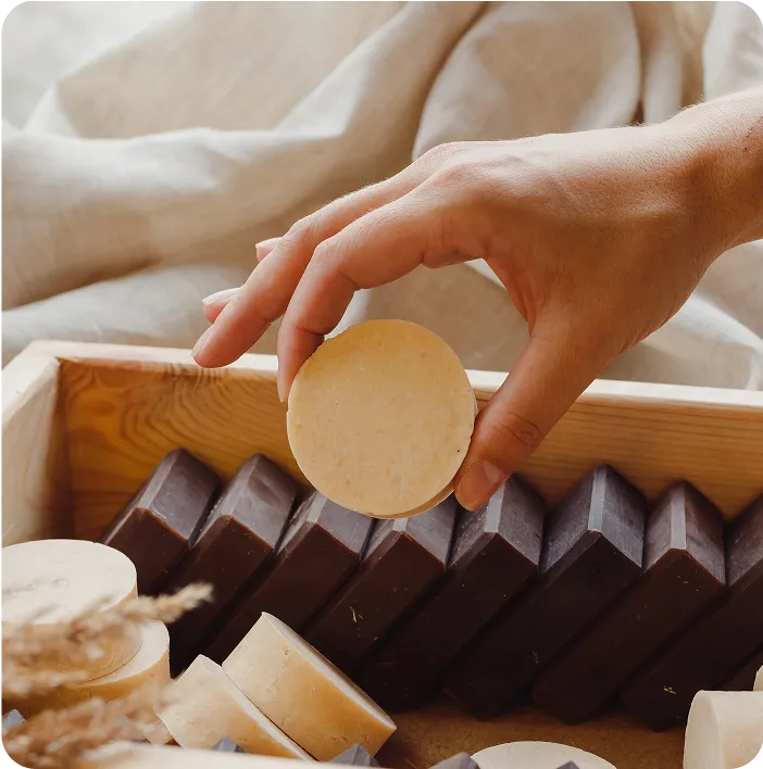 Hand picking a natural solid soap bar from a wooden box, symbolizing eco-friendly, zero-waste cosmetic and packaging solutions.