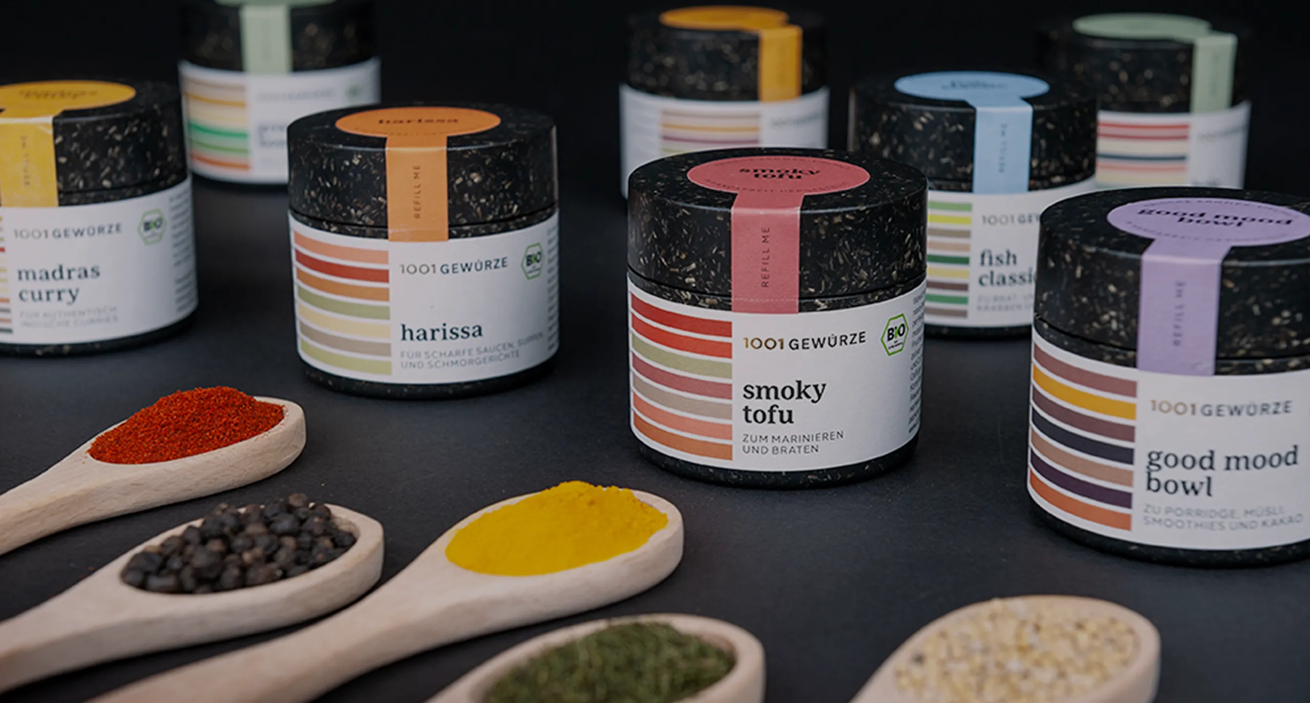 Eco-friendly spice jars labeled 1001 Gewürze with colorful labels and wooden spoons filled with spices, highlighting sustainable packaging and natural ingredients.