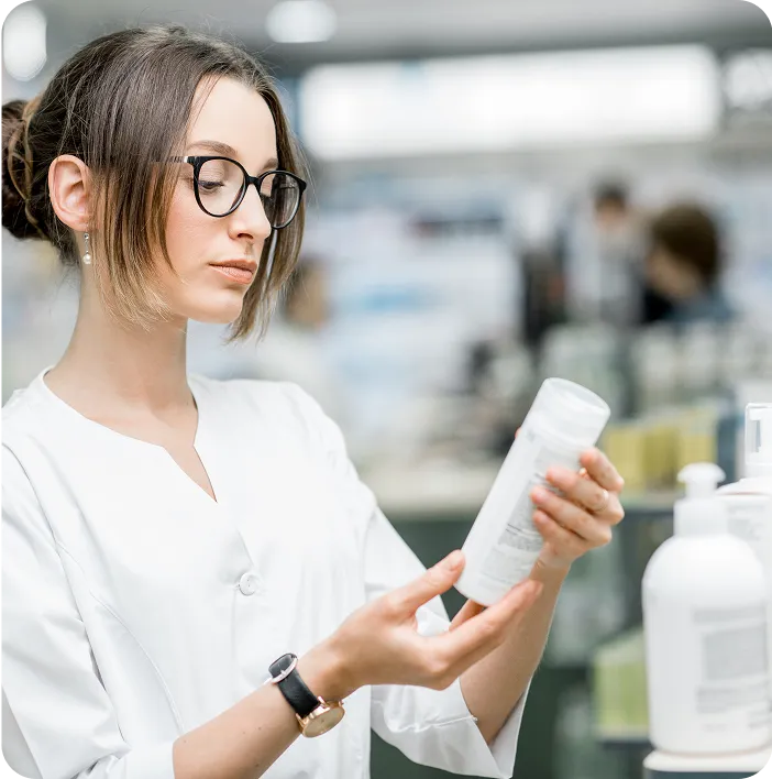 Pharmacist or lab specialist in a white coat examining a product bottle in a pharmacy, representing product quality inspection and professional healthcare environment.