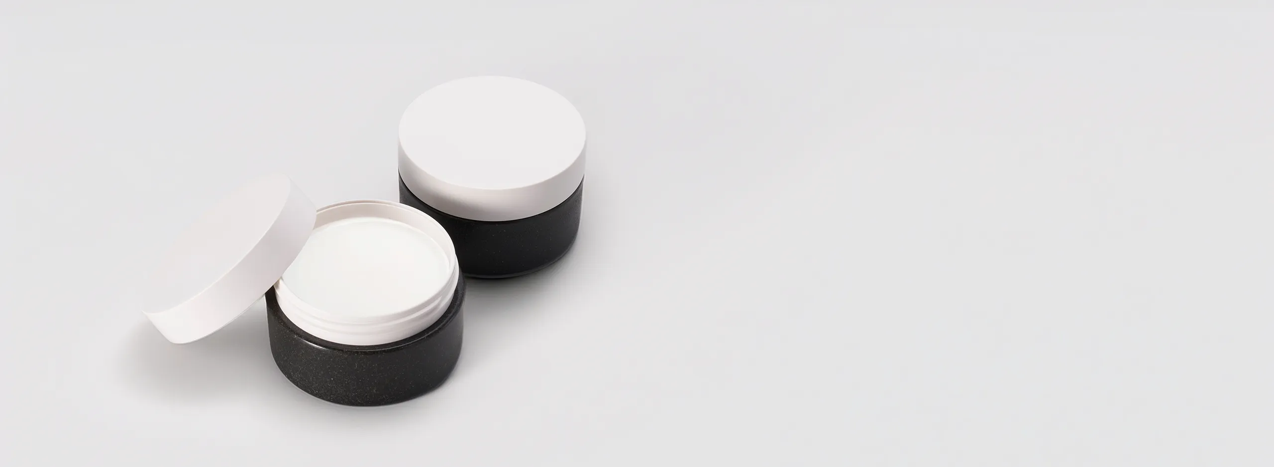 Minimalist cosmetic cream jars with white lids and black eco-friendly bases, showcasing premium sustainable skincare packaging design on light background.