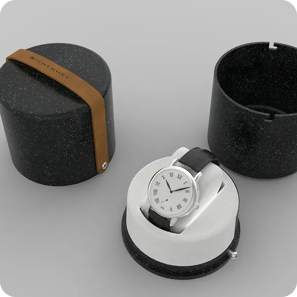 Luxury watch in eco-friendly black cylindrical packaging with Richemont logo and leather strap detail, showcasing sustainable premium design.