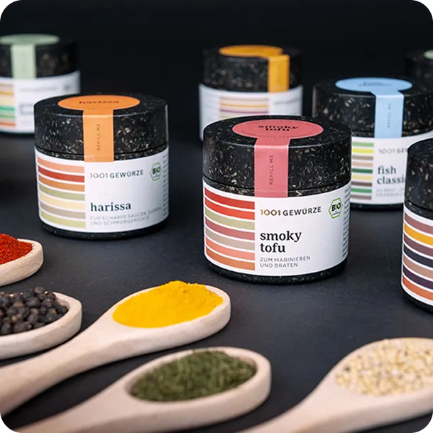 Eco-friendly spice jars from 1001 Gewürze with colorful labels and wooden spoons filled with spices, showcasing sustainable and stylish food packaging design.