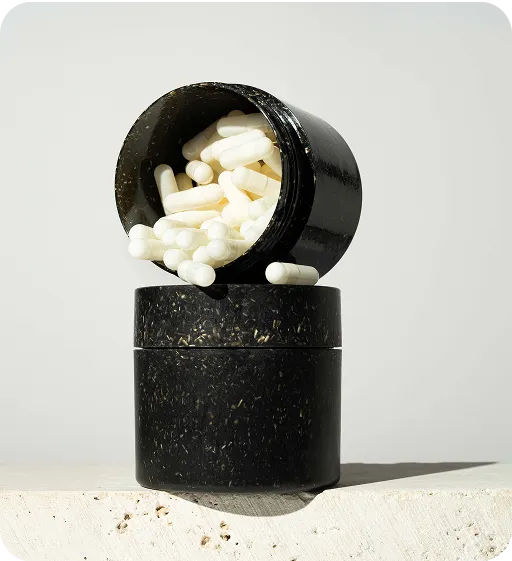 Black sustainable supplement jar made from natural materials with white capsules spilling out, minimalist eco-friendly packaging design.