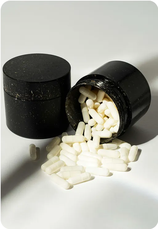Black eco-friendly supplement jar made from natural material with white capsules spilling out, minimalist sustainable packaging design.